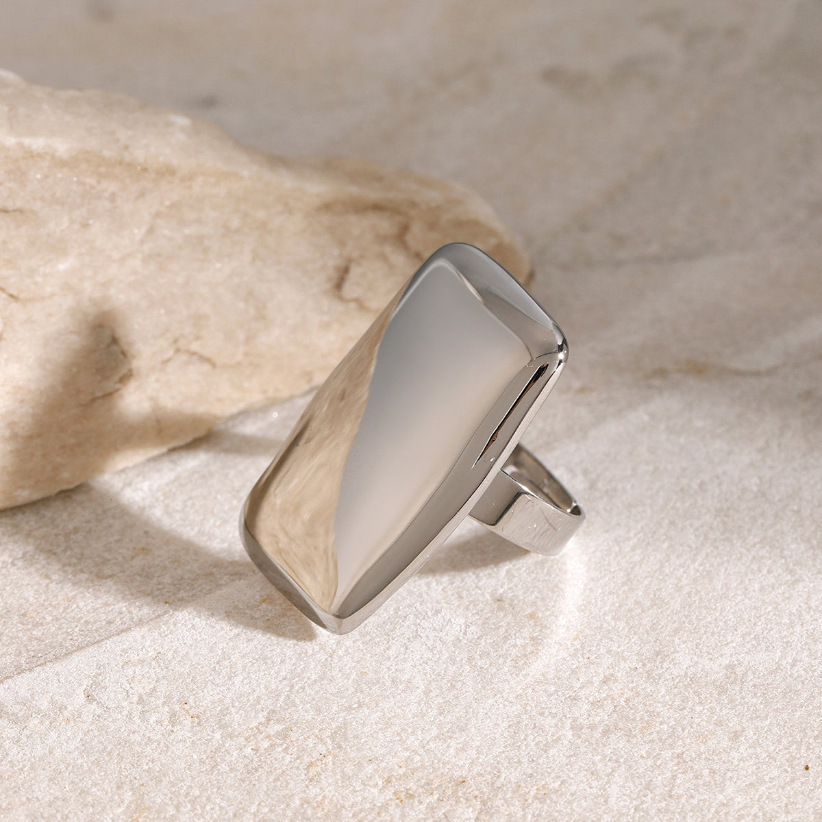 Stainless steel rectangle adjustable open ring on textured surface.