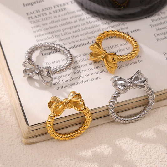 Twisted titanium steel bow rings in platinum and 18K gold plating displayed on a book.