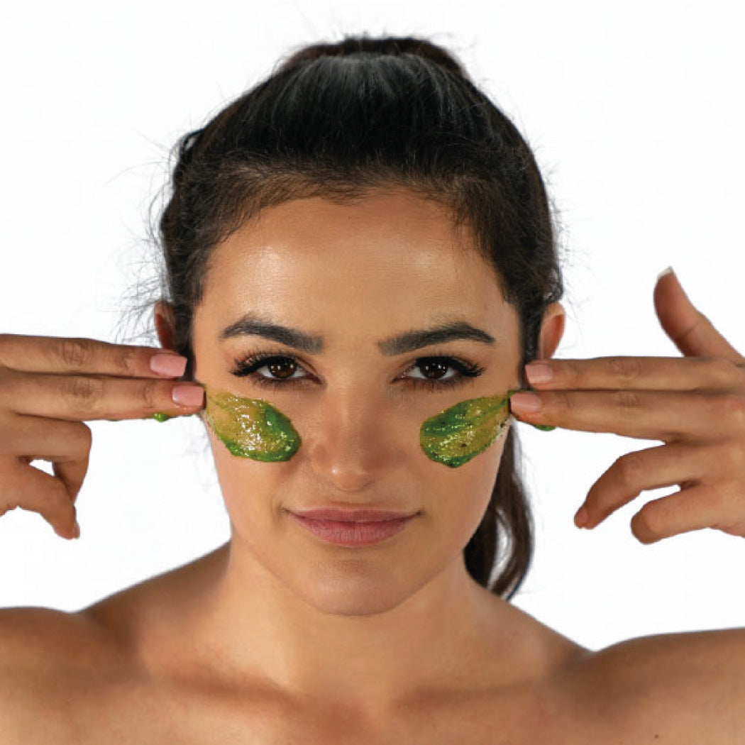 Woman applying green exfoliating mask on cheeks.